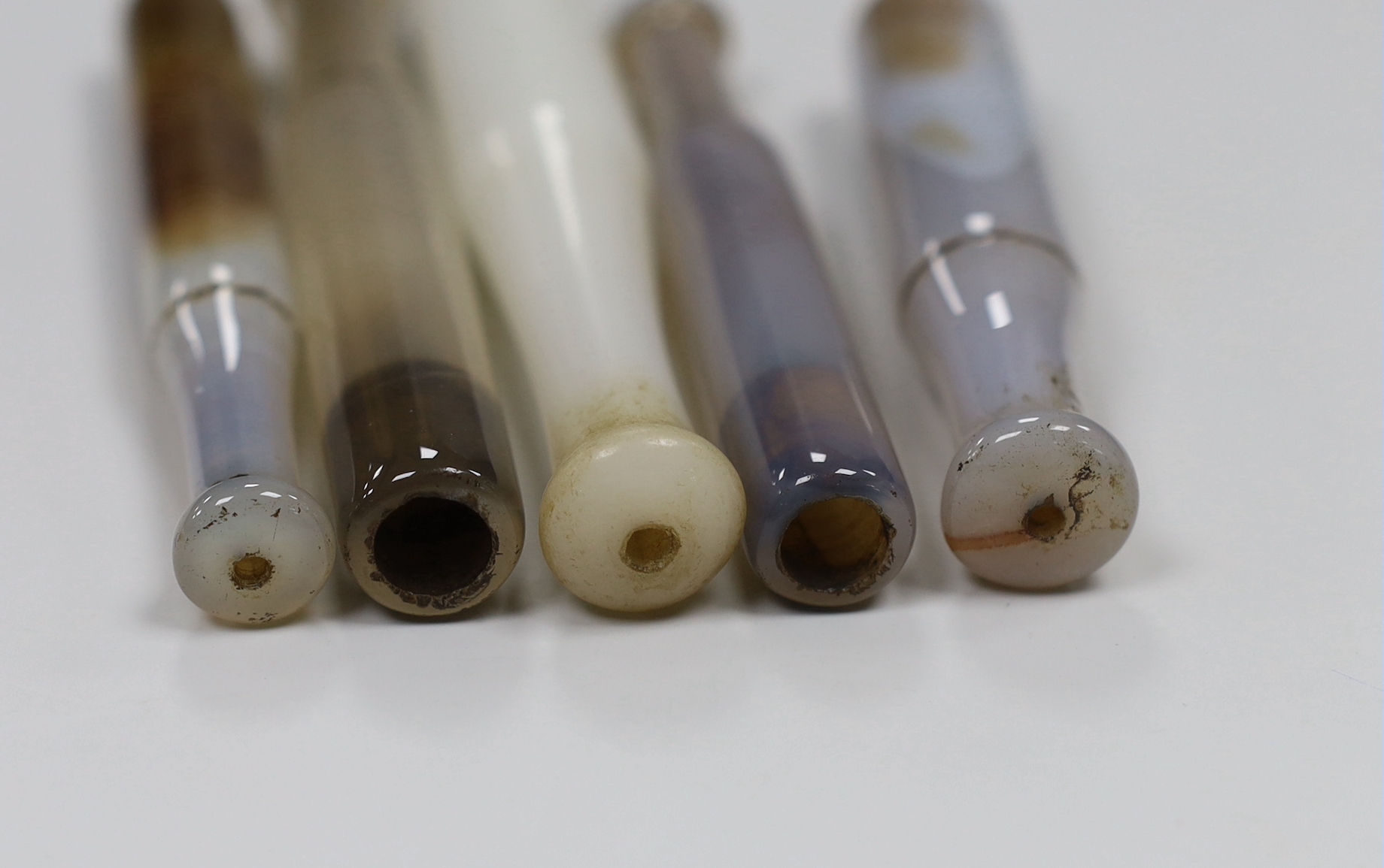 Four Chinese agate opium pipe mouthpieces and a similar glass example, largest 13cm high (5)